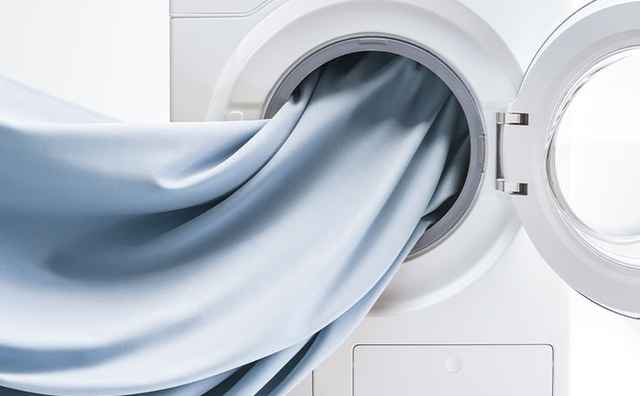 Stoff in Pastellblau wird in die offene Trommel einer Waschmaschine gegeben.