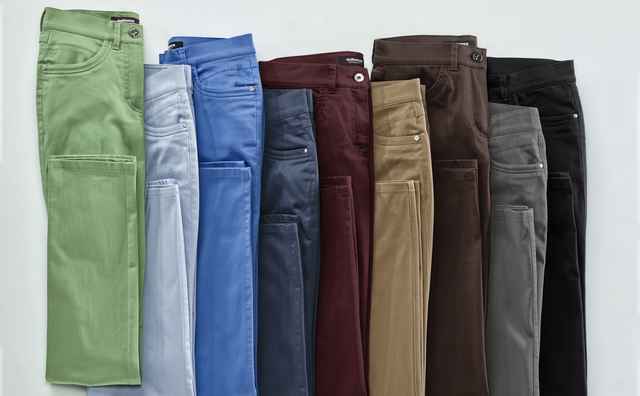 Acht paar gefaltete Hosen in verschiedenen Farben: grün, hellblau, blau, dunkelblau, burgunderrot, braun, grau und schwarz auf weißem Hintergrund.