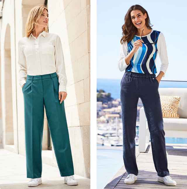 Zwei Frauen in legerer Kleidung posieren draußen; eine trägt eine weiße Bluse und grüne Hose, die andere ein blau-weißes Oberteil und dunkle Hose.