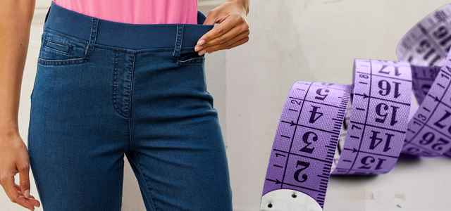 Person trägt blaue Jeans mit elastischem Bund, daneben ein lila Maßband.