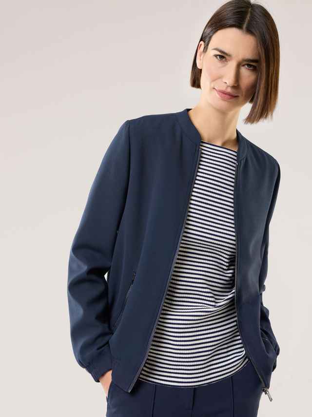 Eine Frau trägt eine dunkelblaue Jacke über einem blau‑weiß gestreiften Oberteil.