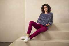 Eine Frau trägt einen bunten Strickpullover, dazu eine rote Hose und weiße Sneaker.