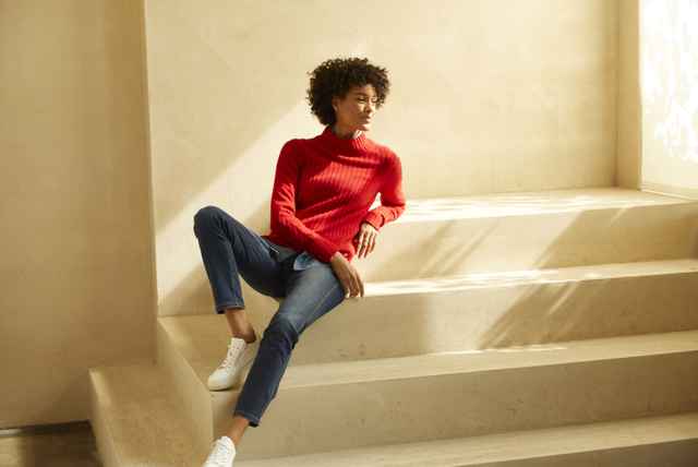 Frau sitz glücklich auf einer Treppe in ihrem roten Cashmere-Pullover