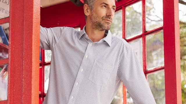 Mann in gestreiftem Hemd steht in einer roten Telefonzelle mit Büchern