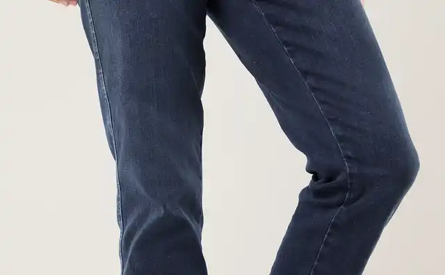 Person in dunkelblauer Jeans und grünem Shirt, trägt blaue Turnschuhe mit weißen Schnürsenkeln, posiert mit gebeugtem Bein.