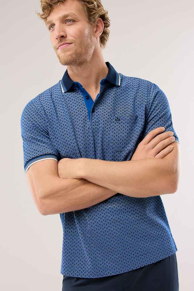 Mann mit lockigem Haar trägt ein blaues Polohemd mit Muster und verschränkten Armen.