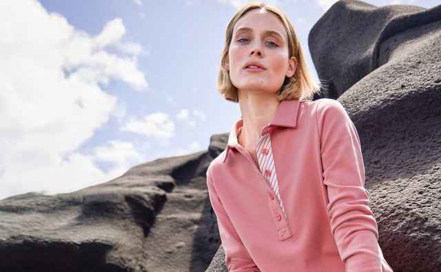 Rosa Polo mit klassischem Kragen, Knopfleiste und aufgesetzten Brusttaschen, kombiniert mit einem gestreiften Oberteil. Der Stil wirkt modern und lässig.