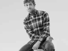 Ein Mann trägt ein kariertes Hemd, dazu eine Jeans.