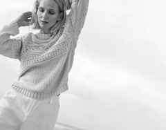 Eine Frau trägt einen gestrickten Pullover mit Muster, dazu eine helle Hose.