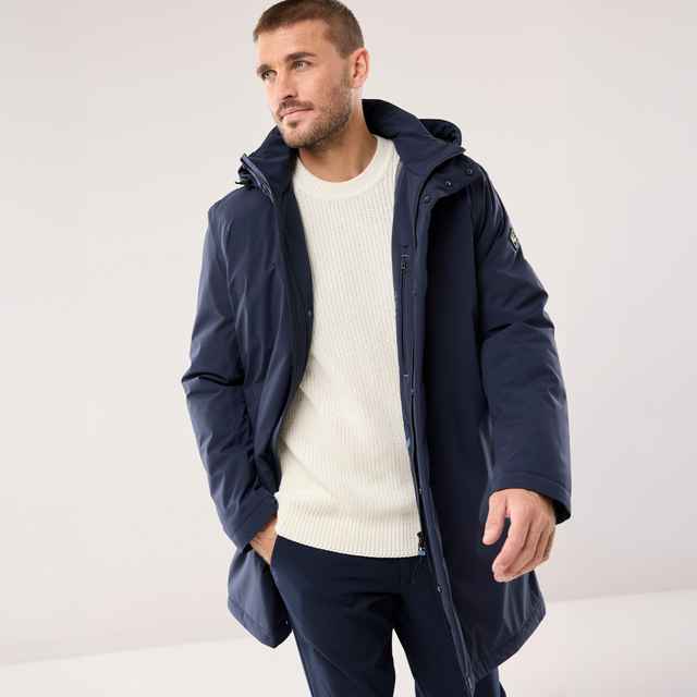 Dunkelblauer Parka mit Kapuze über einem cremefarbenen Strickpullover und einer dunklen Hose. Der Stil ist modern, sportlich und wintertauglich.